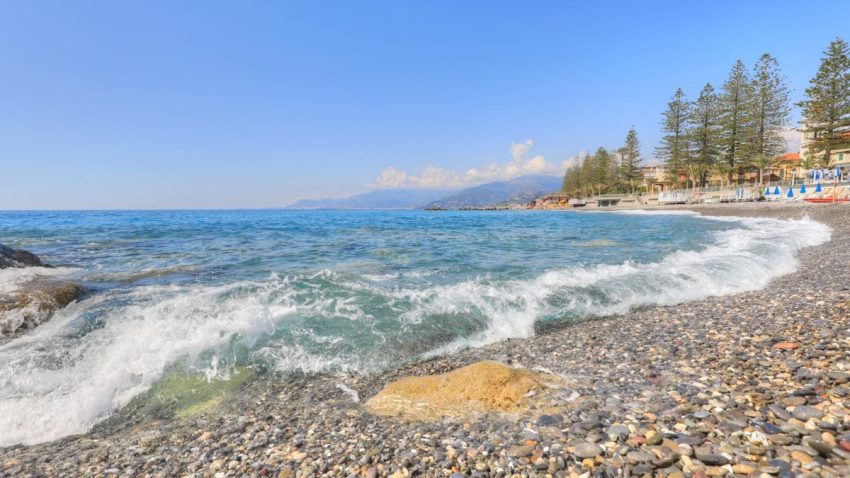 Picturesque view of Bordighera beach with clear azure waters and pebbles under a bright summer sky.